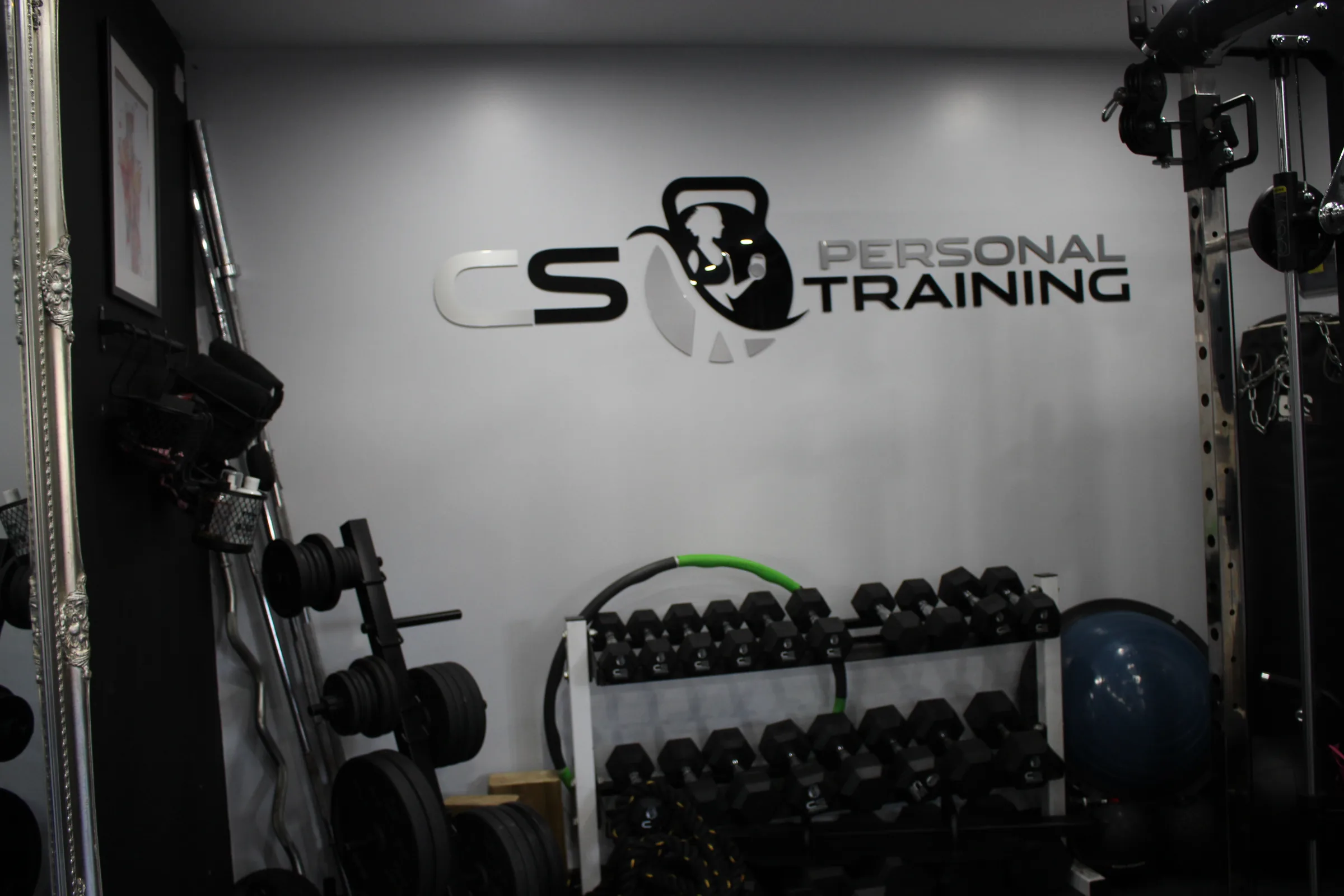 The private studio at Village Way, racks and dumbbells, with the CS Personal Training logo on the wall.