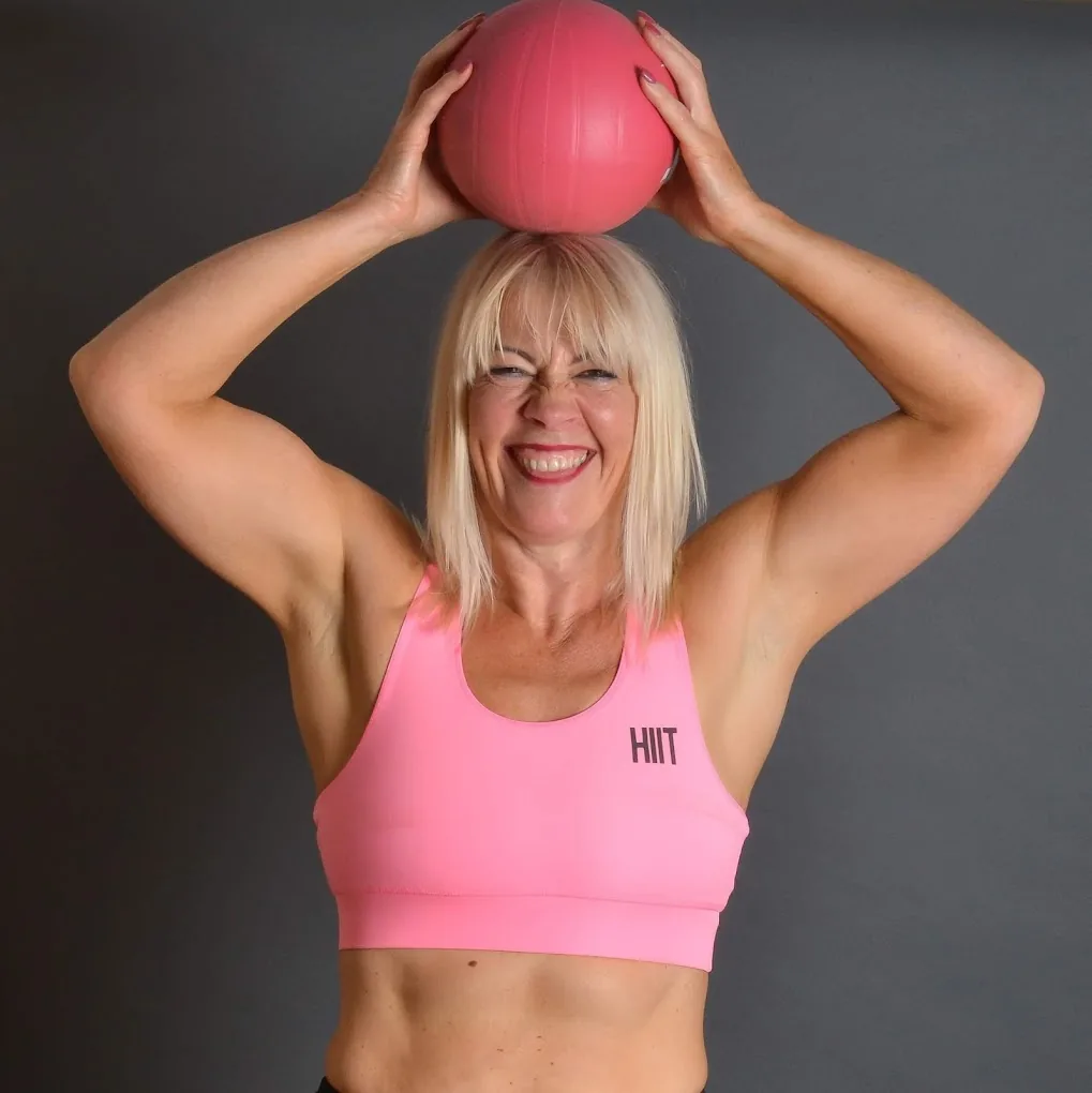 Carol holding a medicine ball overhead in the studio.