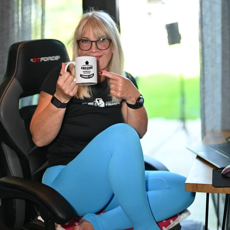 Carol at her desk holding a mug that reads this is what an awesome personal trainer looks like.